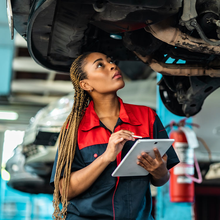 African female tyre fitment worker inspecting wheel alignment with tablet